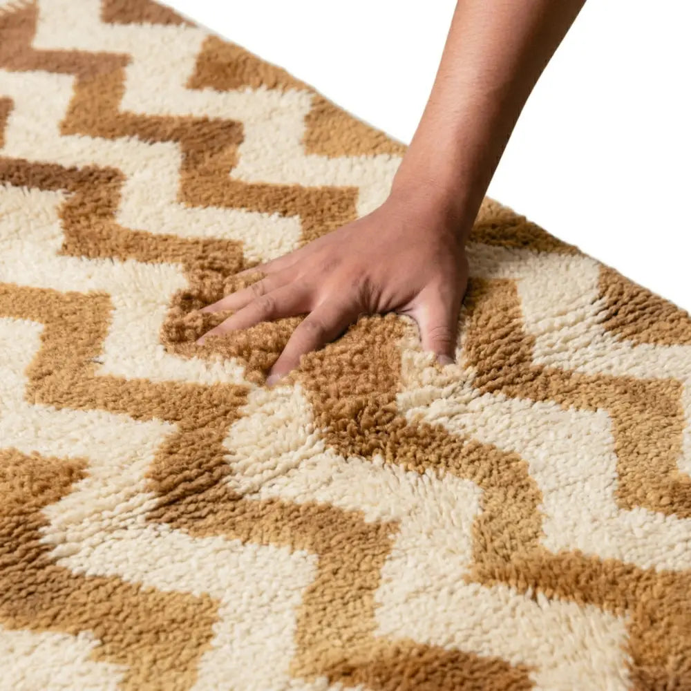 Main appuyant sur tapis berbère beige et marron illustrant confort et densité de la laine