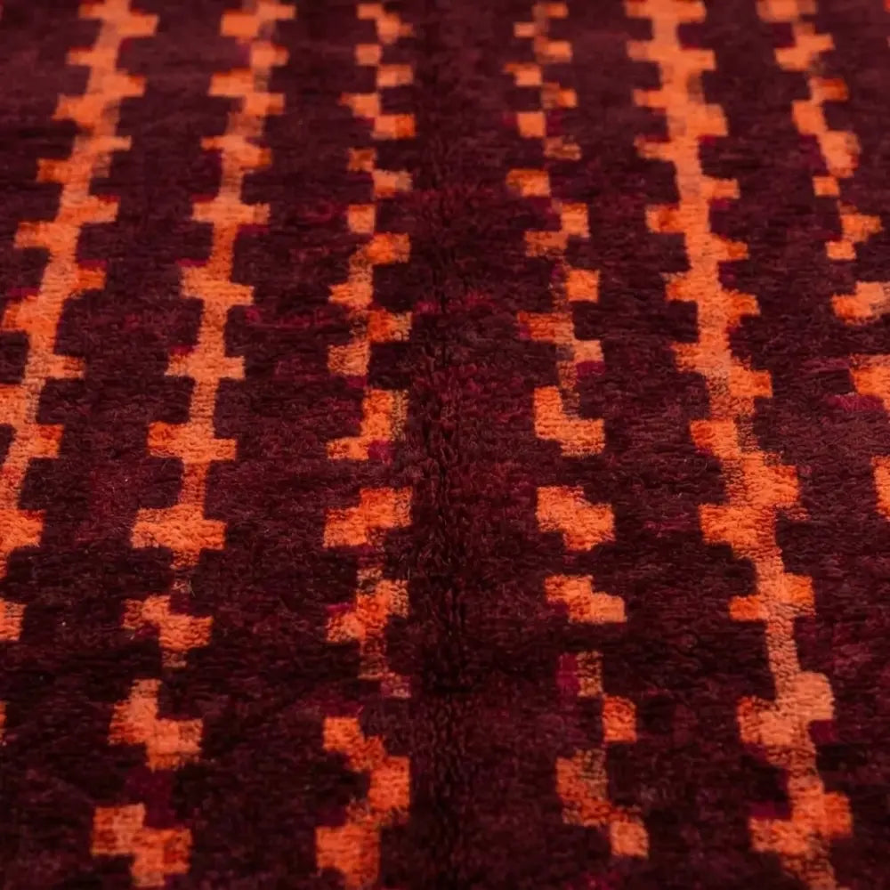 gros plan sur tapis berbère bordeaux avec motifs ethniques orange, texture dense et finition artisanale haut de gamme