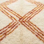 Gros plan tapis berbère crème avec lignes zigzag orange texture laine épaisse artisanale marocaine