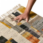 Main appuyant sur tapis berbère géométrique multicolore montrant texture épaisse et douce en laine