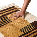 Main appuyant sur tapis berbère ocre à motifs géométriques montrant texture épaisse et moelleuse en laine