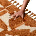Main sur tapis berbère ocre et écru en laine moelleuse, confort premium et qualité haut de gamme