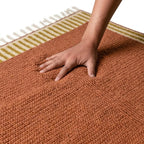 Main sur tapis berbère ocre en laine épaisse, toucher moelleux et qualité haut de gamme