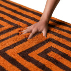 Main sur tapis berbère en laine douce à rayures orange et marron, texture épaisse et confort haut de gamme