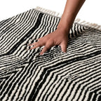 Main sur tapis berbère noir et blanc en laine épaisse, texture douce et confort haut de gamme