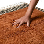 Main sur tapis berbère ocre en laine épaisse, texture moelleuse et qualité artisanale haut de gamme