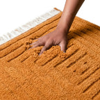 Main sur tapis berbère orange en laine douce avec relief géométrique, confort premium et finition artisanale