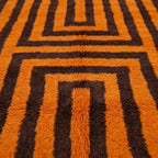 Gros plan sur tapis berbère motif géométrique orange et marron, finition artisanale et design contemporain