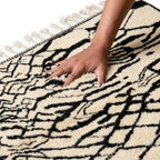 Main appuyant sur tapis berbère noir et blanc texture douce et moelleuse laine artisanale haut de gamme