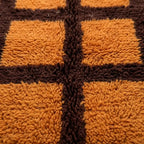 Gros plan tapis berbère orange avec motifs carreaux marron texture laine épaisse artisanale marocaine