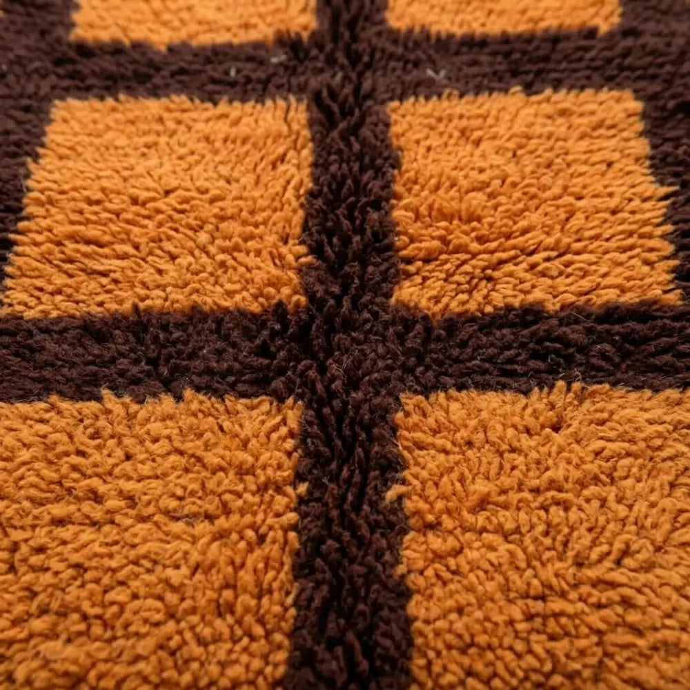 Gros plan tapis berbère orange avec motifs carreaux marron texture laine épaisse artisanale marocaine