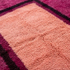 Gros plan sur tapis berbère rose avec centre pêche, mettant en valeur le tissage artisanal et la douceur des fibres naturelles