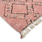 Détail des franges et motifs d’un tapis berbère rose, mettant en avant une finition artisanale de qualité et un design unique