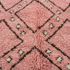 Tapis berbère rose avec motifs géométriques noirs et détails écrus, texture douce en laine pour une décoration chaleureuse et tendance