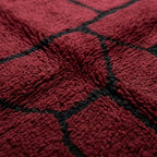 Gros plan sur tapis berbère rouge avec motifs noirs, mettant en valeur le tissage artisanal et la qualité de la laine naturelle