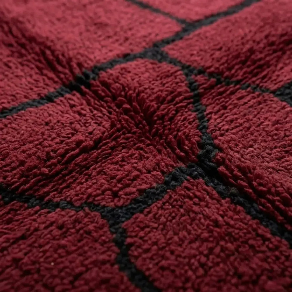 Gros plan sur tapis berbère rouge avec motifs noirs, mettant en valeur le tissage artisanal et la qualité de la laine naturelle