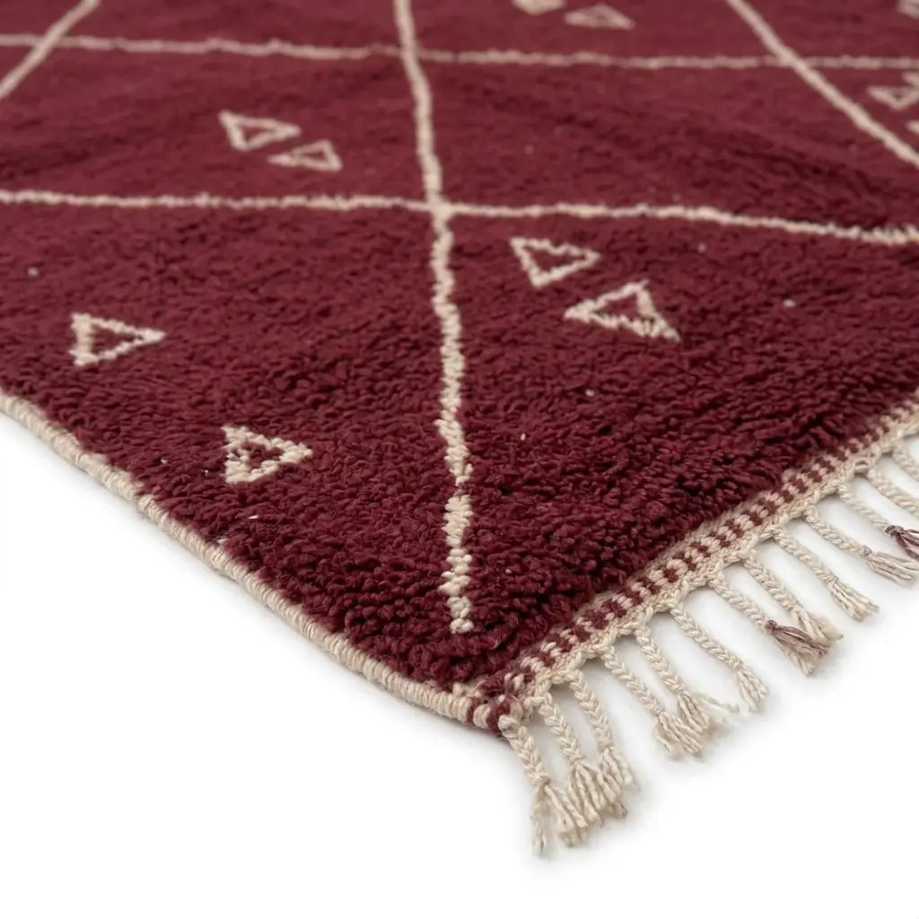 Détail des franges d’un tapis berbère rouge avec motifs blancs, soulignant une finition artisanale haut de gamme et durable