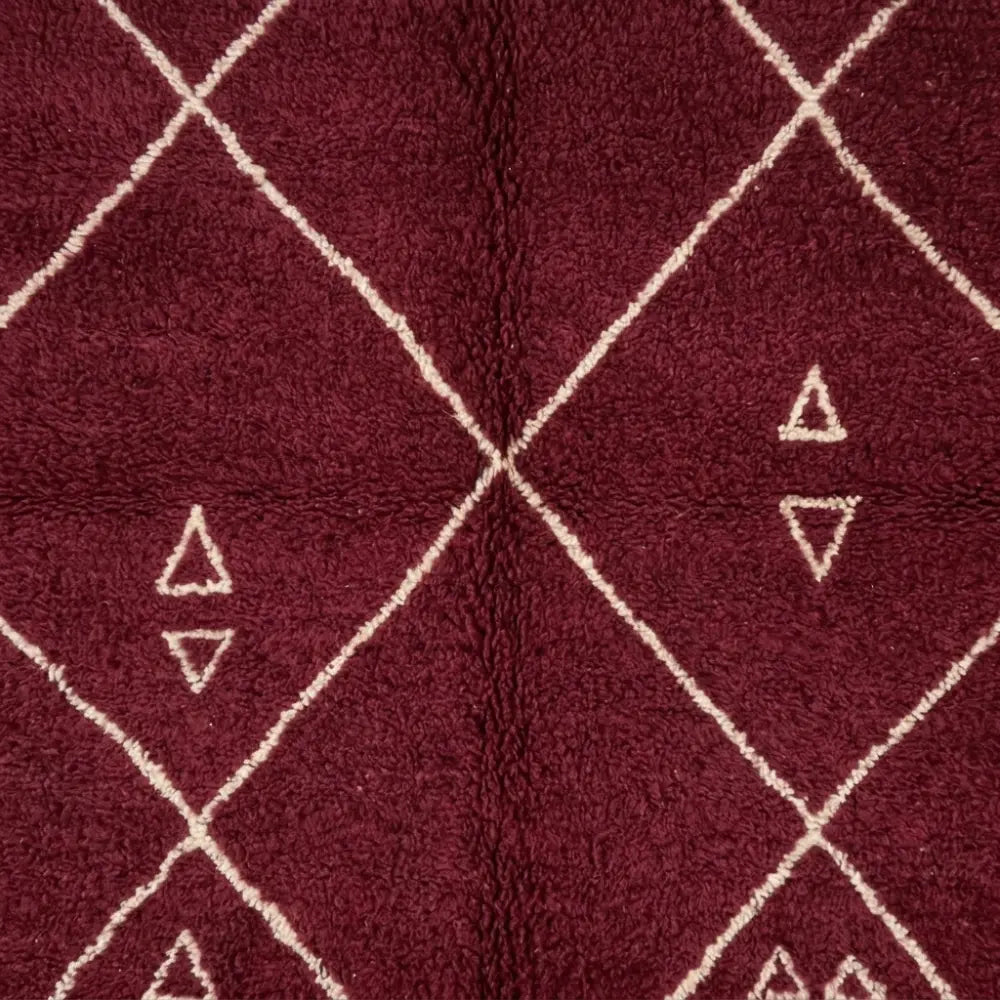 Gros plan sur tapis berbère rouge avec motifs blancs, mettant en valeur le savoir-faire artisanal et la qualité de la laine