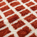 Gros plan tapis berbère terracotta à motifs carreaux sur fond crème texture laine épaisse artisanat marocain