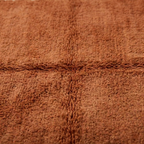 gros plan sur tapis berbère terracotta avec relief central subtil et fibres épaisses, finition artisanale haut de gamme