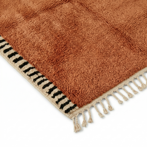 coin de tapis berbère terracotta avec franges écrues et bordure à motifs noirs, idéal pour intérieur chaleureux et tendance