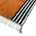 Détail tapis berbère terracotta avec franges blanches et bordures rayées finition artisanale haut de gamme