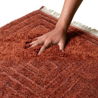 main enfoncée dans tapis berbère terracotta à motif géométrique en relief, texture épaisse et ultra douce pour confort premium
