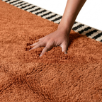 main enfoncée dans tapis berbère terracotta à poils longs avec bordures graphiques noir et blanc, texture ultra douce et confort premium