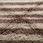 Détail texture tapis berbère fait main avec fibres épaisses et rayures rose et écru, qualité artisanale premium