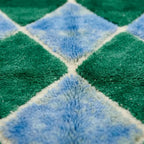 gros plan sur tapis berbère en laine avec motifs losanges vert et bleu, texture épaisse et artisanale haut de gamme