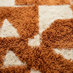 Gros plan sur tapis berbère en laine épaisse avec motifs abstraits ocre et écru, texture douce et artisanale