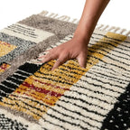 Main sur tapis berbère en laine épaisse avec motifs géométriques multicolores, texture douce et haut de gamme