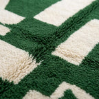 Gros plan sur la texture épaisse en laine d’un tapis berbère vert et blanc à motifs abstraits