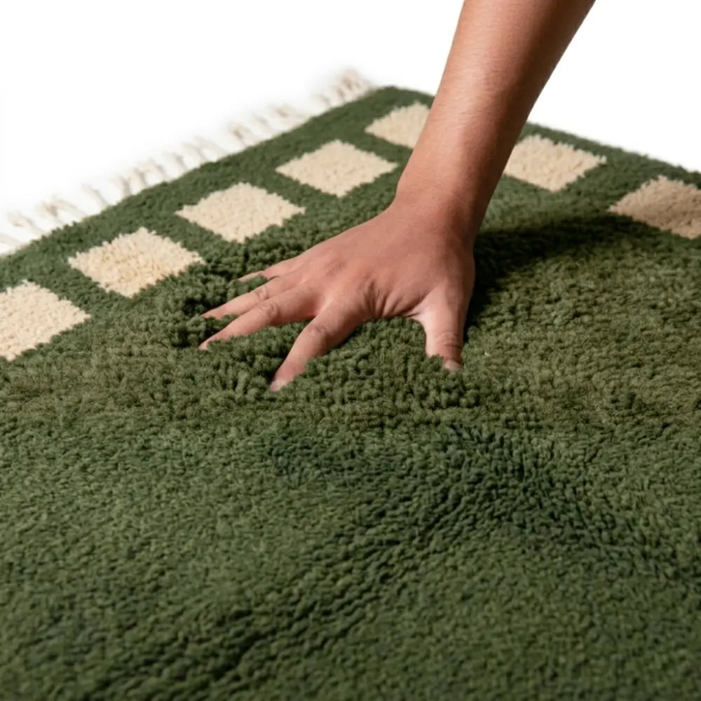 main enfoncée dans tapis berbère vert à carrés beiges, texture épaisse et moelleuse offrant confort premium et douceur