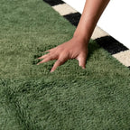 Main pressant un tapis berbère vert moelleux et épais, texture douce et confortable idéale pour décoration intérieure moderne