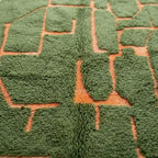 détail tapis berbère vert avec motif géométrique abstrait en relief terracotta, texture épaisse et finition artisanale premium