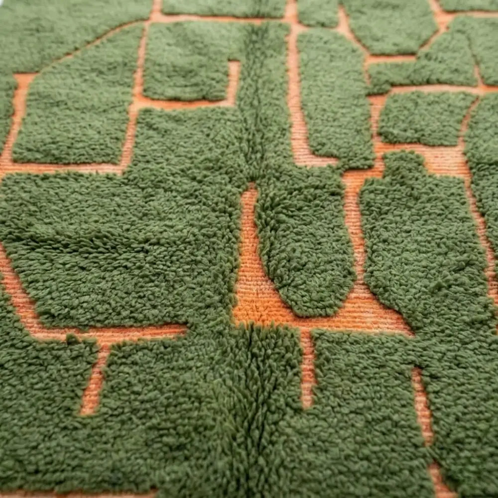 détail tapis berbère vert avec motif géométrique abstrait en relief terracotta, texture épaisse et finition artisanale premium
