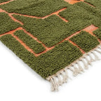 coin de tapis berbère vert avec motifs terracotta en relief et franges blanches, parfait pour décoration intérieure bohème tendance